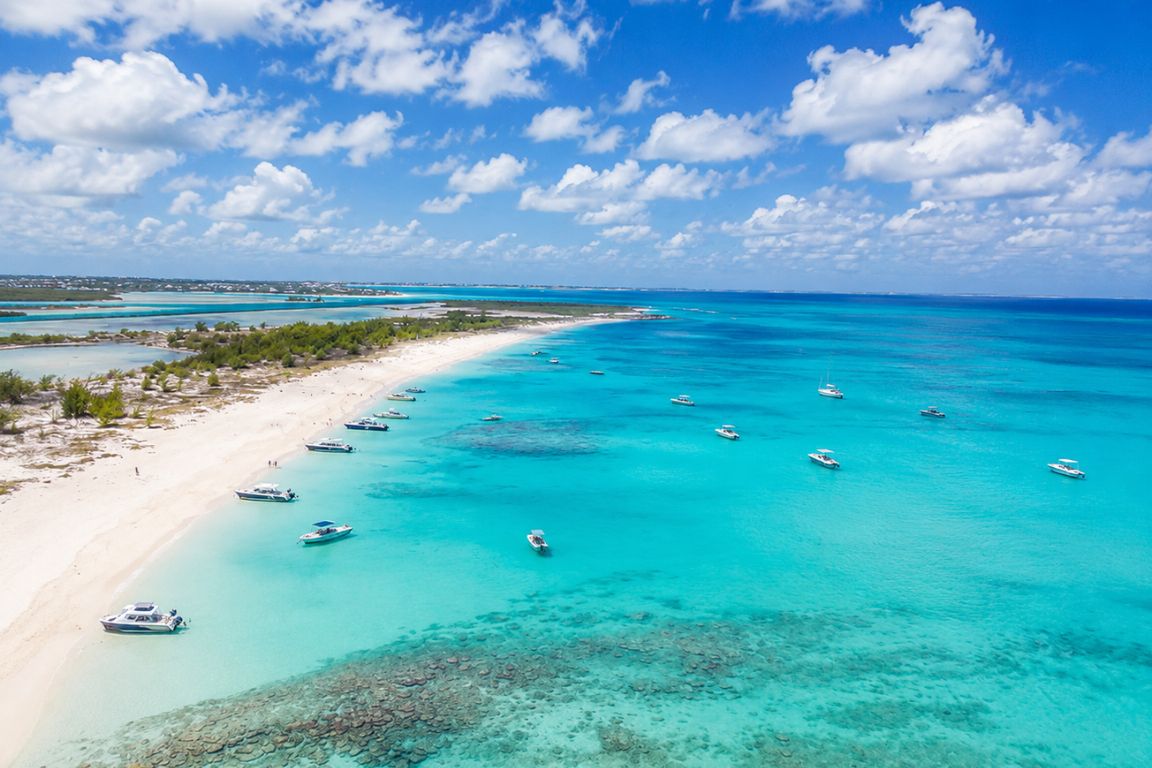 Aerial view of Half Moon Bay with turquoise Caribbean waters, white sand beach, and anchored boats during a guided island tour with Turks and Caicos Tours